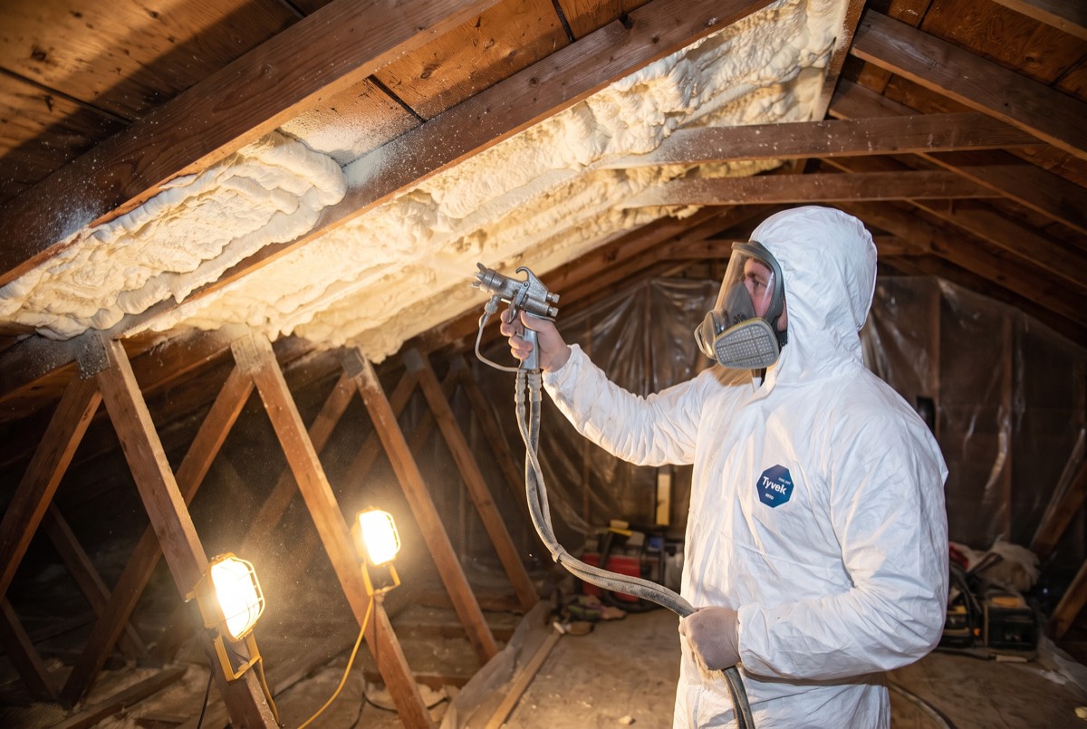 Technician in protective suit spraying foam insulation on an attic roof deck in Anna, TX
