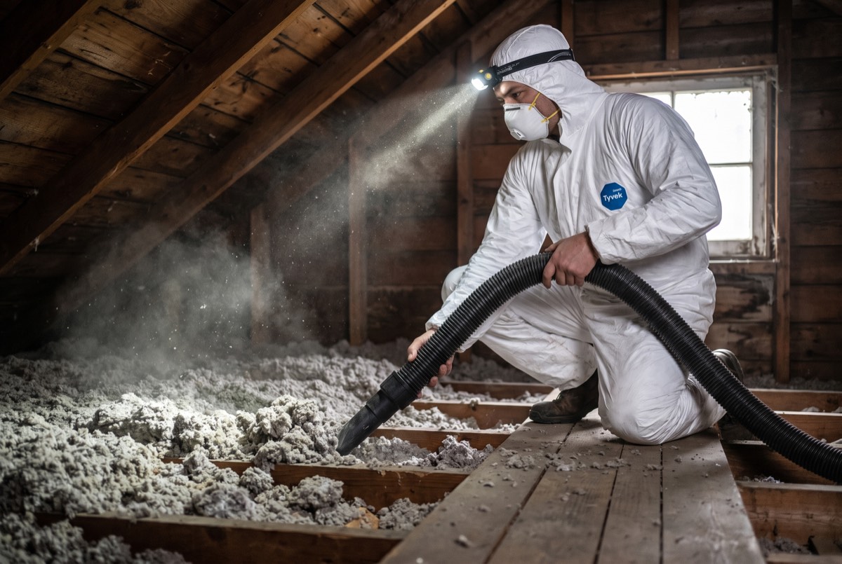 Technician vacuuming old degraded insulation from an attic before spray foam replacement